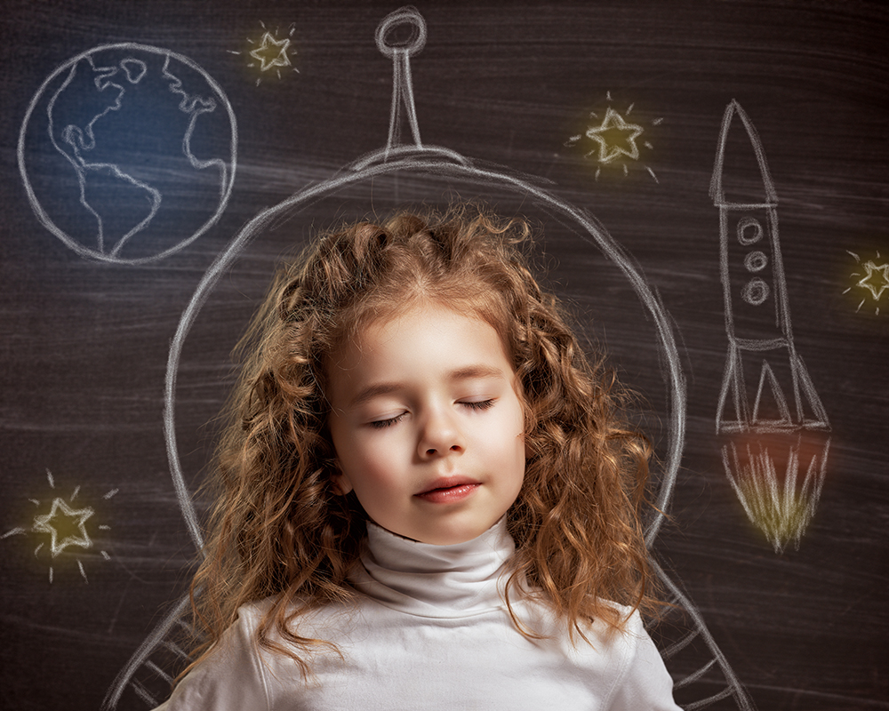 Niña soñando; aparece un dibujo de un cohete, estrellas y el planeta tierra.